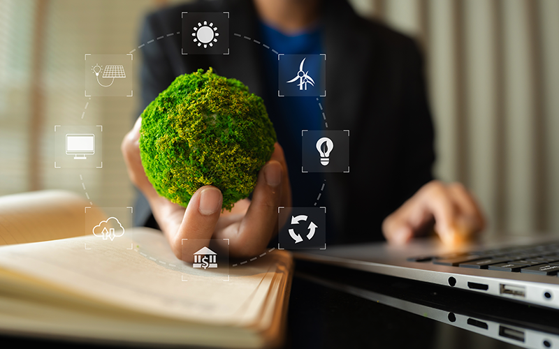 Person mit einer Hand am Laptop. In der anderen Hand hält sie eine grüne Kugel, die die Erde symbolisiert