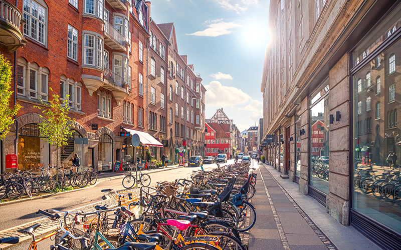 Blick in eine Straße in Kopenhagen, links und rechts sind Häuser. Am Straßenrand sind viele Fahrräder abgestellt