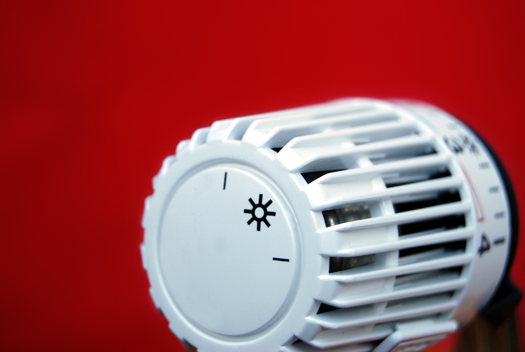 Weißes Thermostatventil vor rotem Hintergrund, Symbol für Energieeinsparung durch richtiges Heizen.