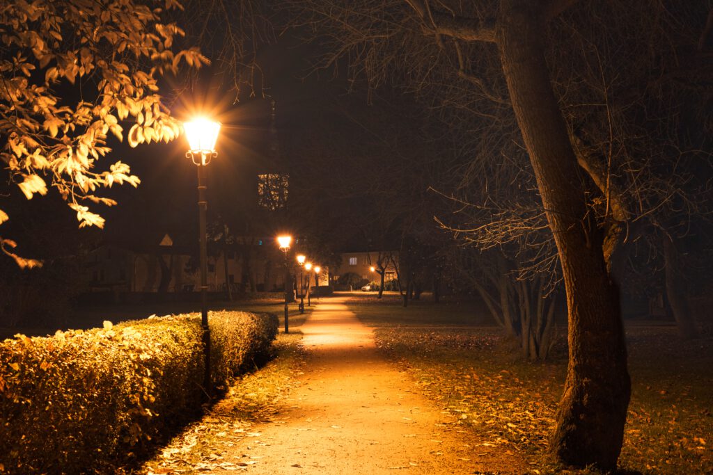 Beleuchteter Gehweg in einem Park bei Nacht mit Straßenlaternen und Bäumen