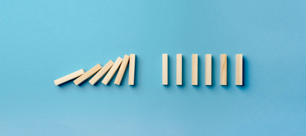 Mehrere Holzklötze stehen aufrecht. Einige Klötze fallen um wie Dominosteine. Daneben stehen weitere Klötze stabil.