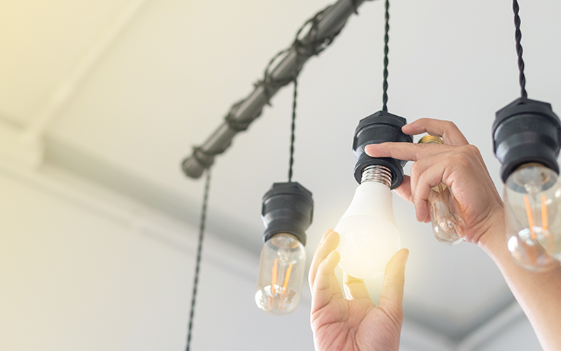 Hände schrauben eine leuchtende Glühbirne in eine Fassung an einer Deckenleuchte mit mehreren Glühbirnen