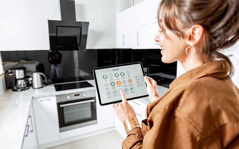 Person steht in moderner Küche und bedient Tablet mit Smart-Home-Steuerungsoberfläche.