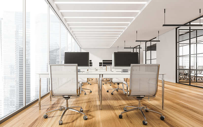 Helles modernes Büro mit großem Tisch, mehreren Computermonitoren und Bürostühlen auf Holzfußboden.