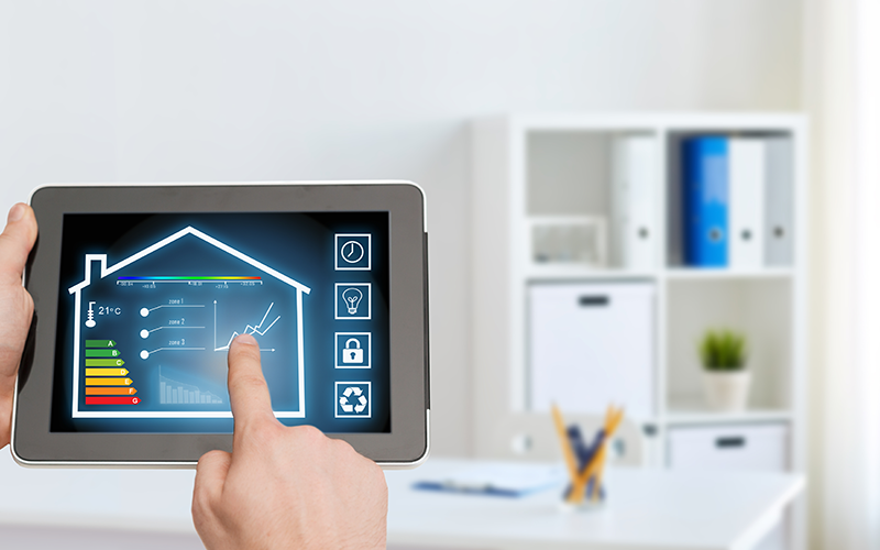 Tablet mit Smart-Home-Dashboard, das Temperatur, Energieeffizienz und Diagramme in Hausform anzeigt, vor unscharfem Bürohintergrund.