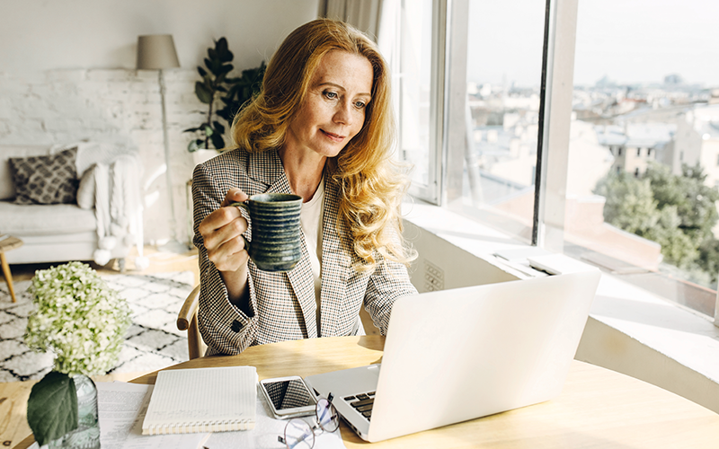 Arbeitssituation im Home-Office. Frau sitzt an einem Tisch im Wohnzimmer und arbeitet an einem Laptop.