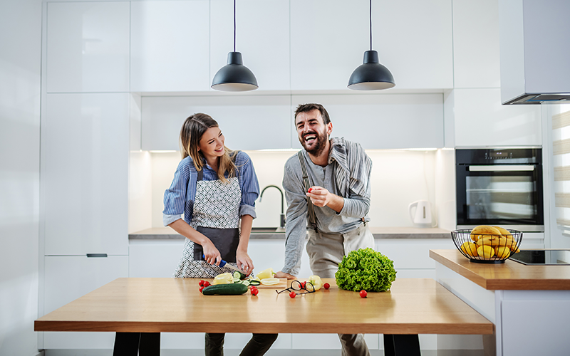 Zwei Personen in einer modernen Küche bereiten Gemüse auf einer Holzarbeitsplatte vor.