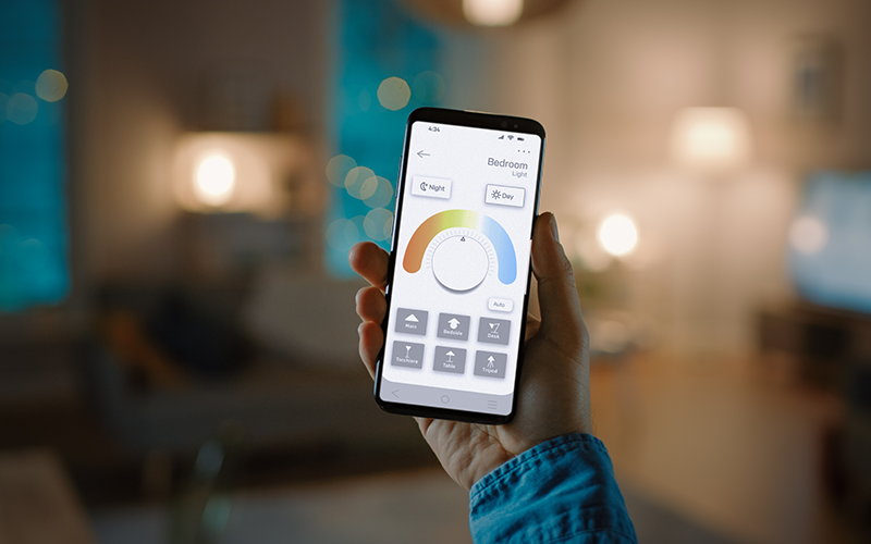 Hand hält Smartphone mit App zur Steuerung der Beleuchtung im Schlafzimmer.