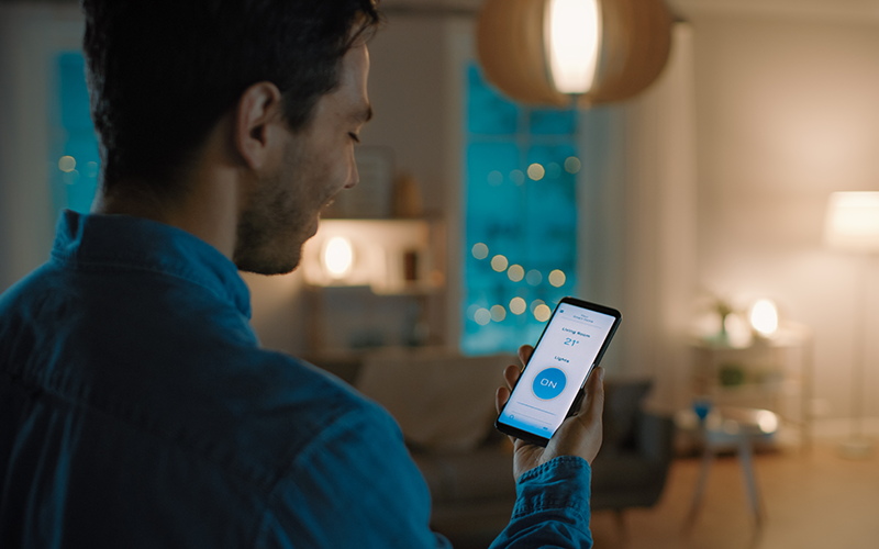 Mann mit Handy, das die digitale Temperatureinstellung der Wohnung anzeigt.