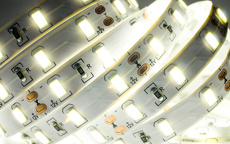 Nahaufnahme eines gebogenen LED-Streifen mit leuchtenden weißen LEDs und sichtbaren elektronischen Bauteilen.