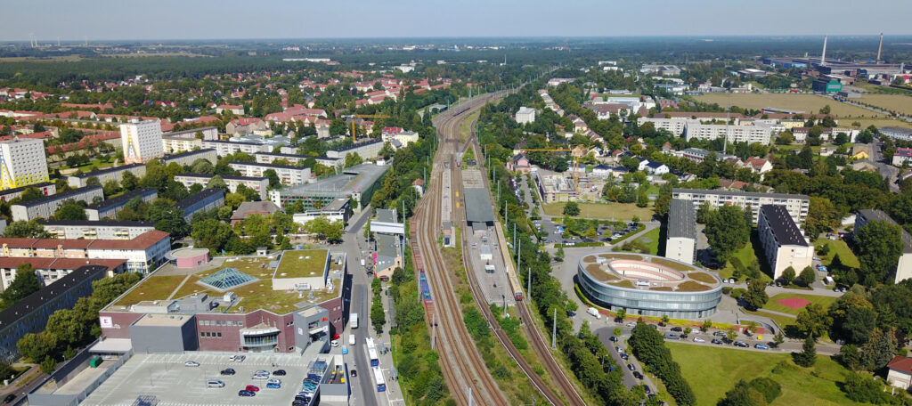 Luftaufnahme von Hennigsdorf mit Wohngebäuden, Bahngleisen, Straßen und vielen Bäumen.