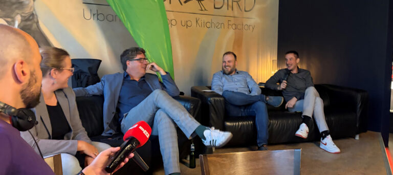 Fünf Männer und eine Frau sitzen bei einem Energiegespräch in lockerer Runde zusammen und lachen. Im Vordergrund ist ein rbb24-Mikrofon zu sehen.