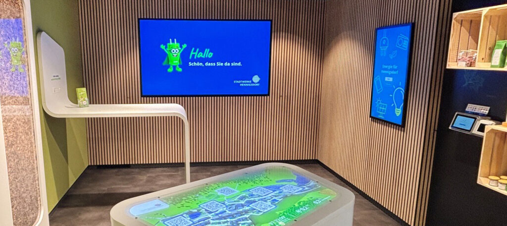 Blick in den Stadtwerke-Shop im ZIEL mit interaktivem AR-Tisch und digitalen Informationsbildschirmen.